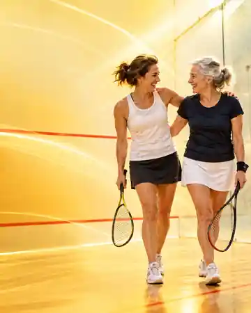 Two adults talking together with squash rackets on court